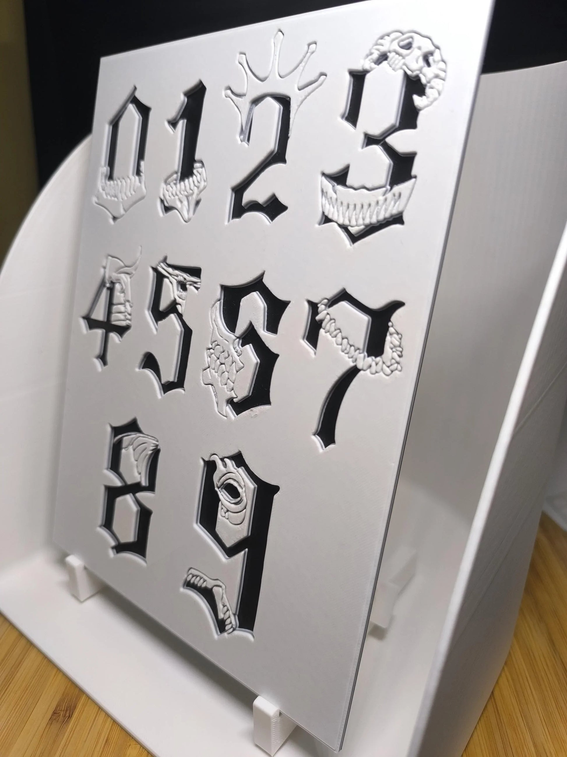 Plastique blanc avec découpe de chiffres gothiques de 0 à 9 et détails en relief, sur support blanc