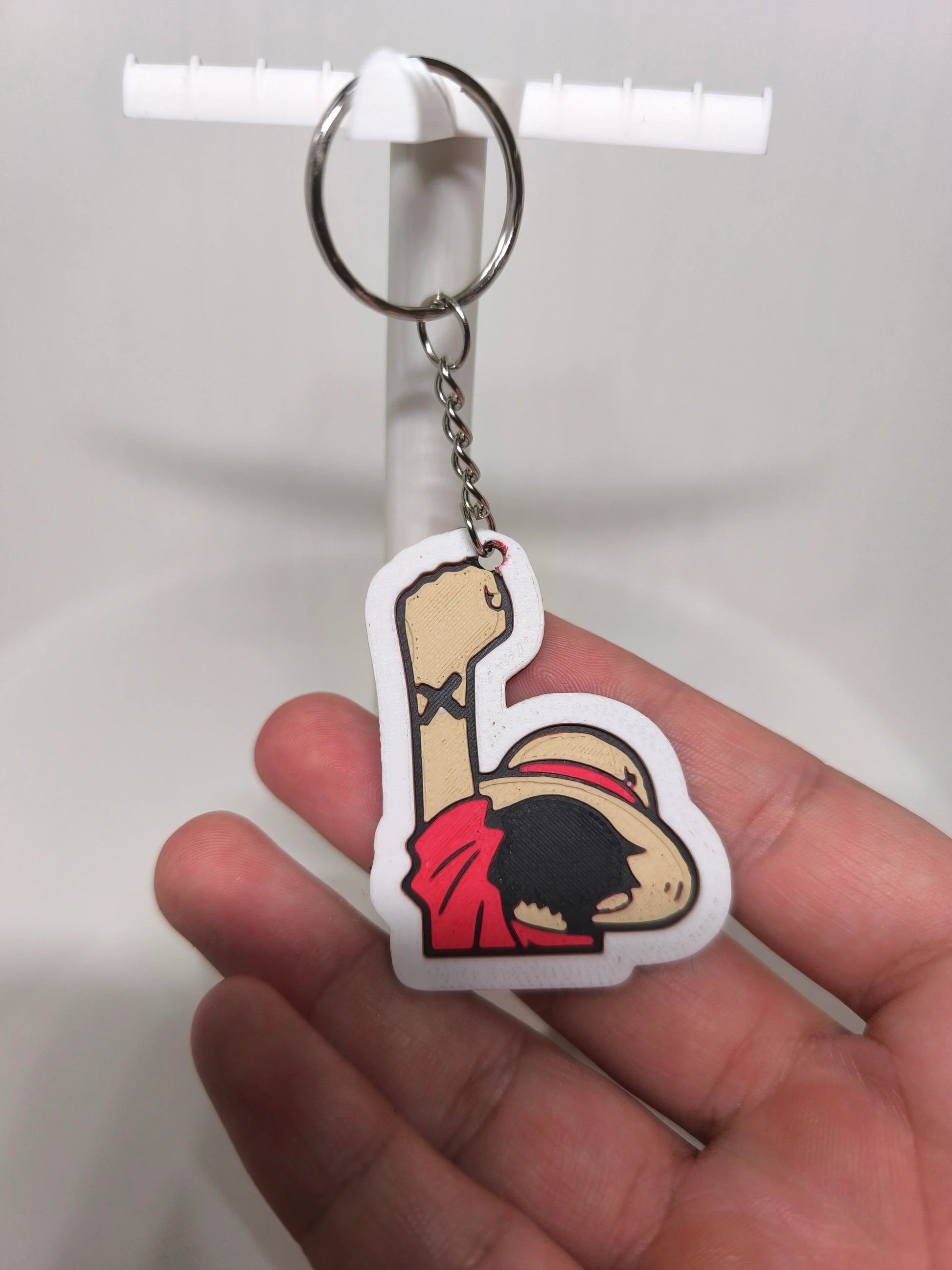 Porte-clés en plastique représentant un personnage cartoon avec chapeau et bras levé, tenu à la main