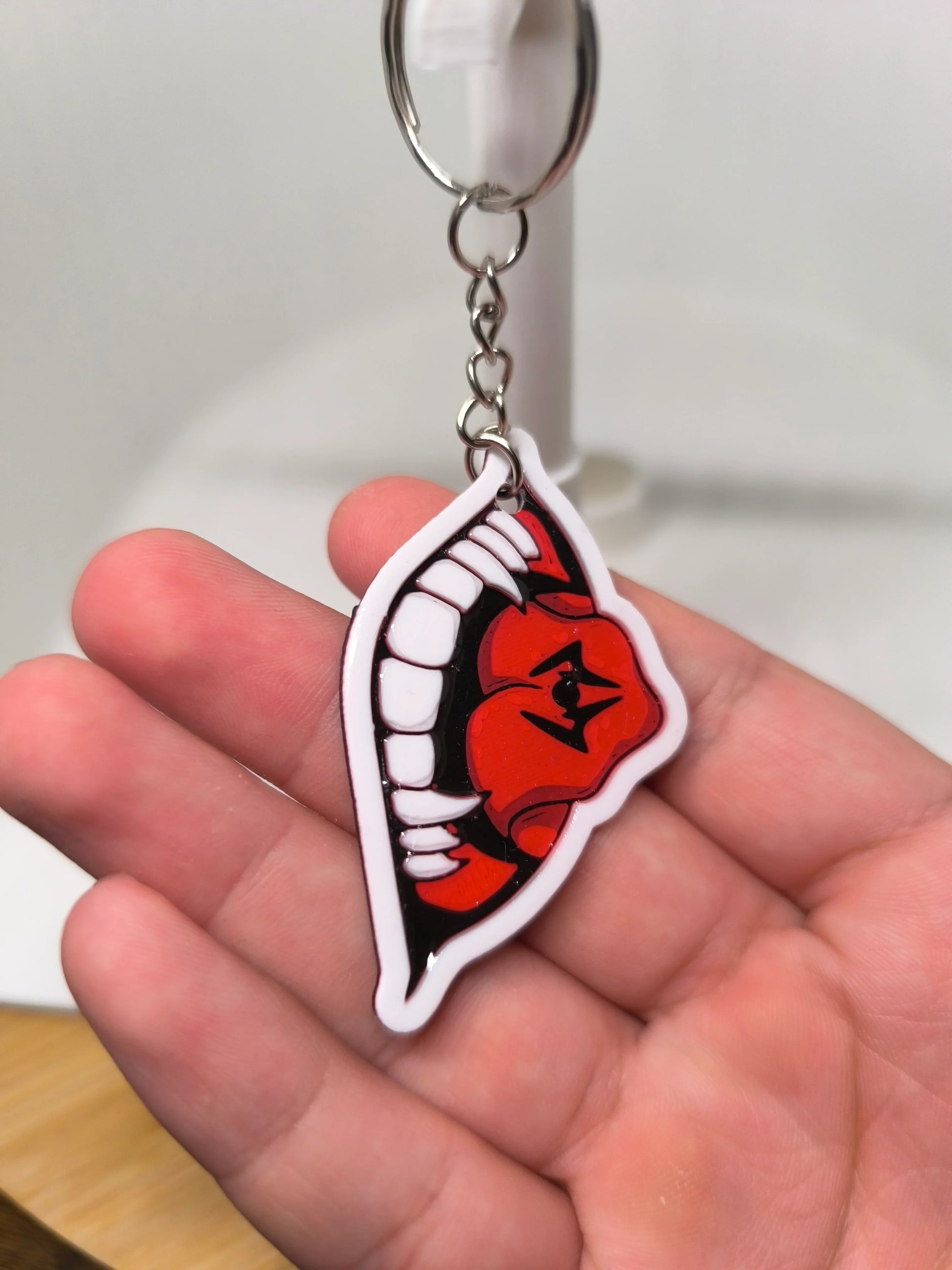 Porte-clés main tenant un design de bouche rouge avec dents blanches pointues sur fond flou