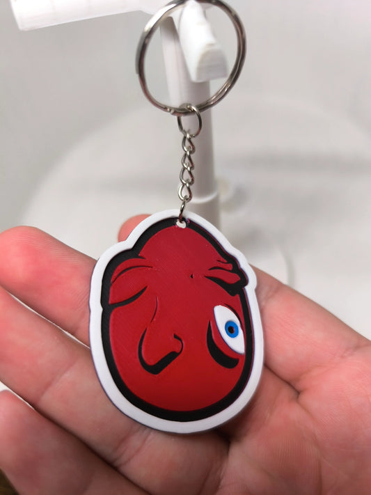 Porte-clés en plastique avec dessin rouge stylisé d'un poisson et œil bleu tenu en main