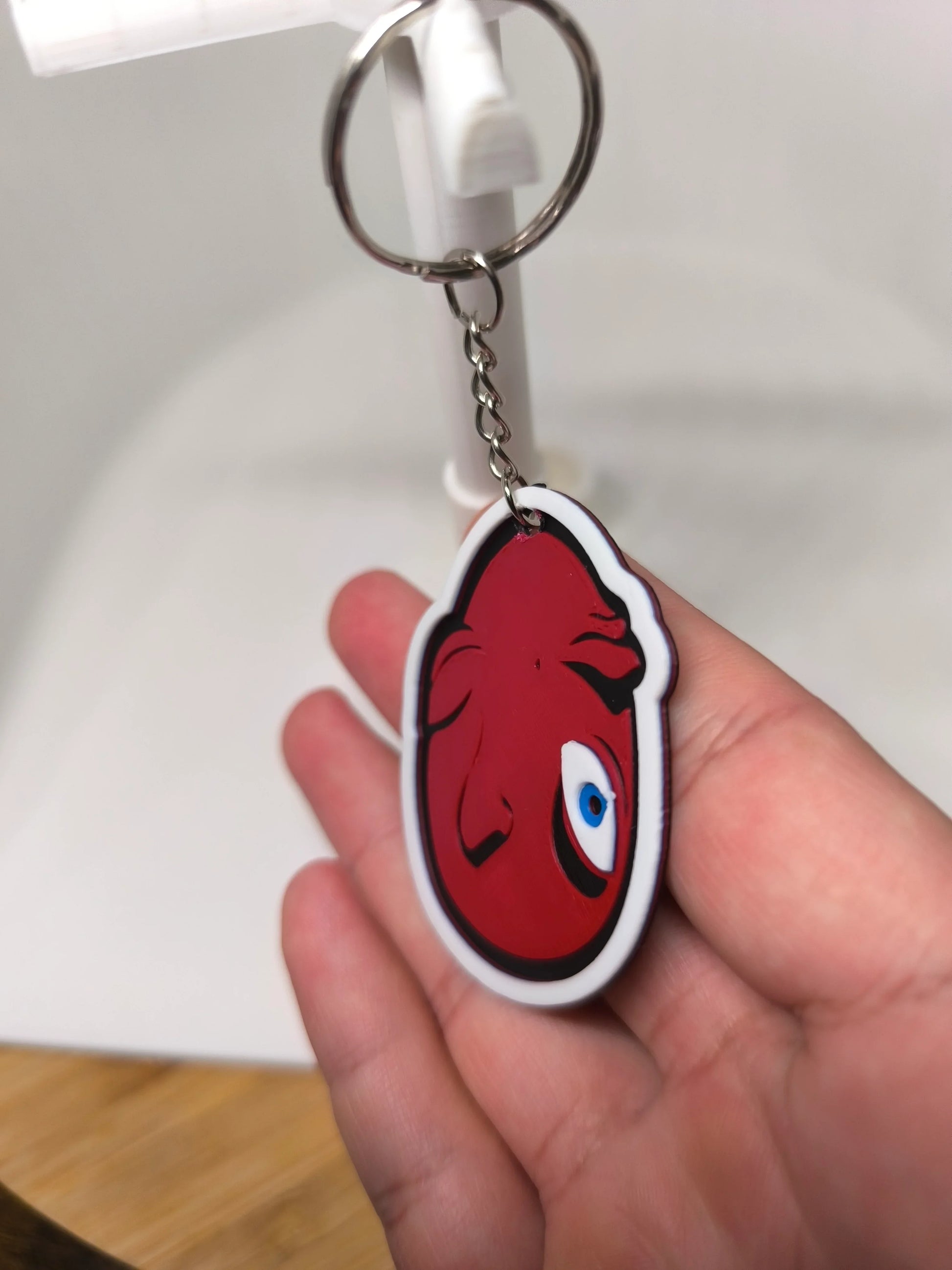 Porte-clés en plastique rouge avec un visage stylisé et un œil bleu, tenu dans une main