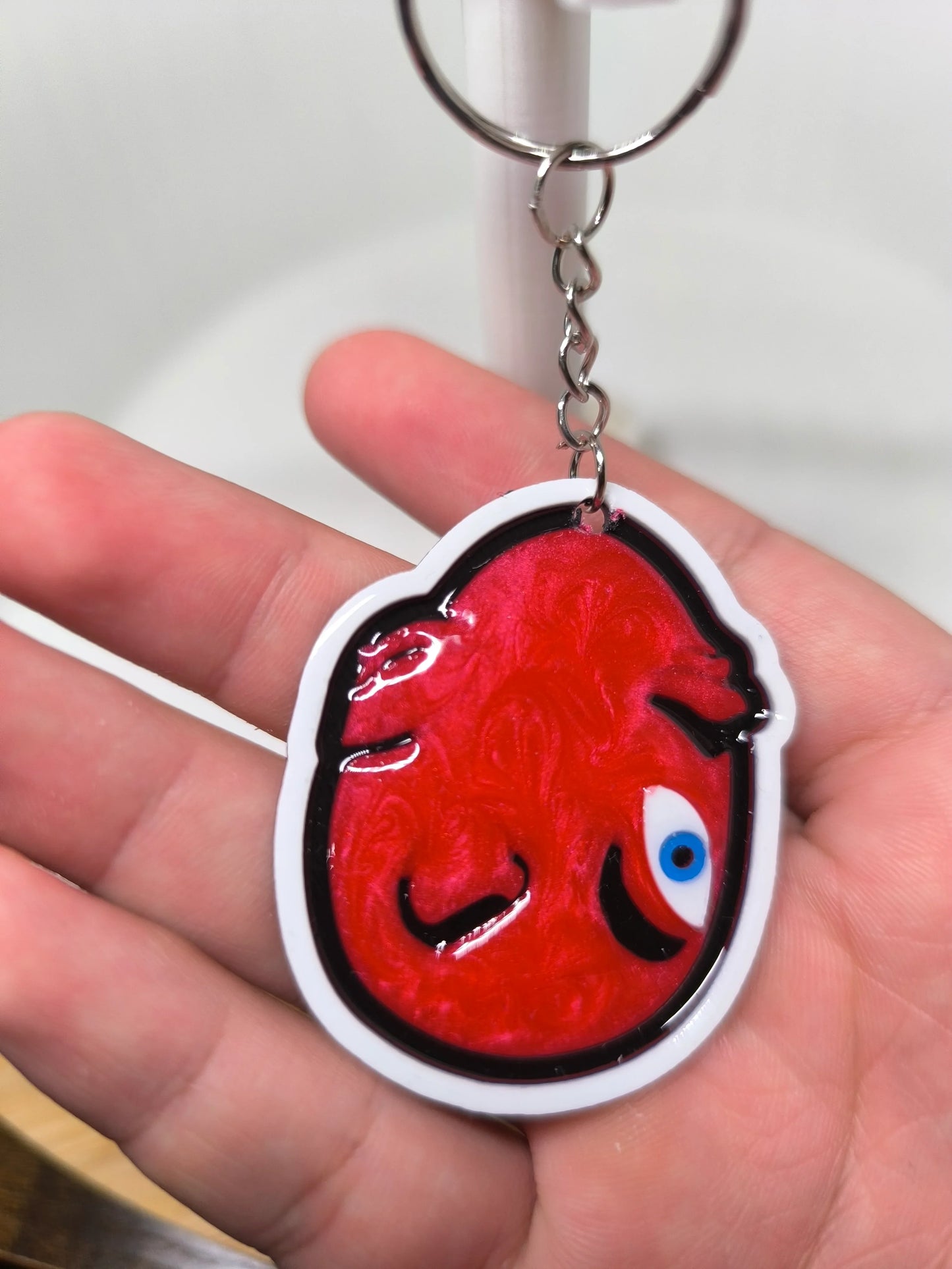Porte-clés en plastique rouge brillant avec visage stylisé et œil bleu tenu dans une main