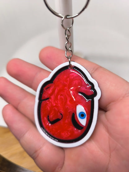 Porte-clés en forme de cœur rouge stylisé avec œil bleu, tenu dans une main