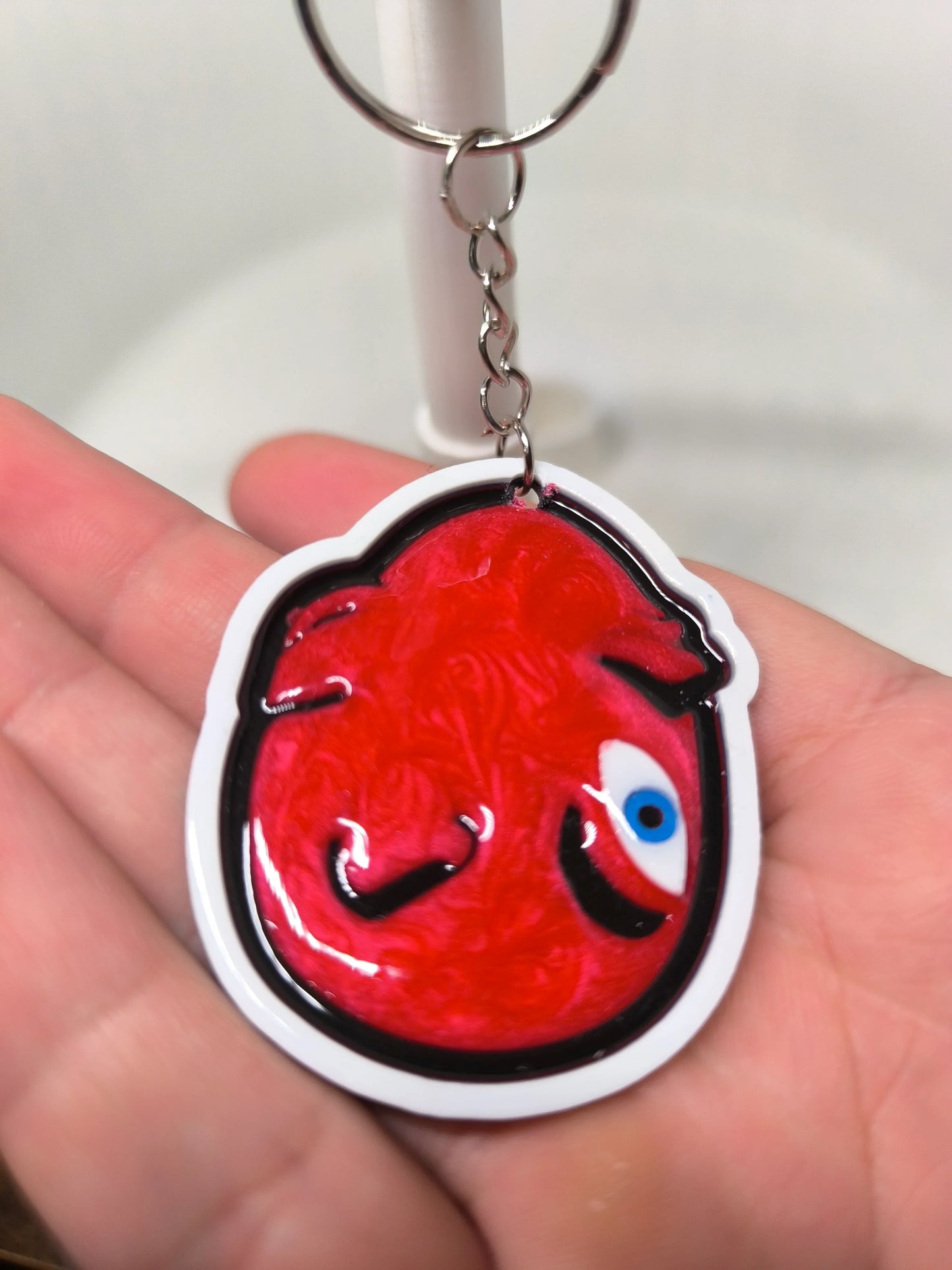 Porte-clés avec dessin rouge abstrait et œil bleu, tenu dans une main