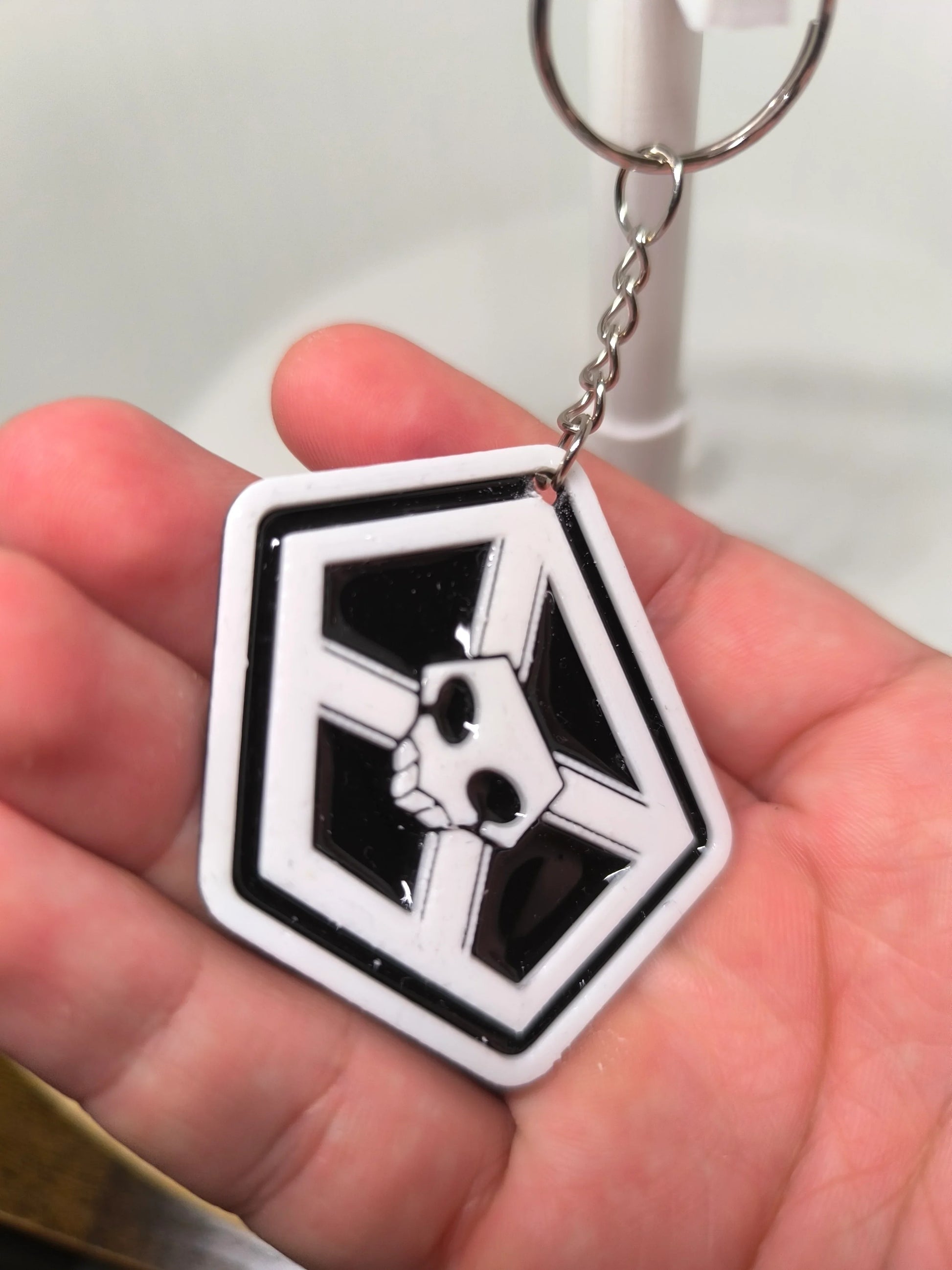 Porte-clés en plastique avec logo noir et blanc et motif crâne tenu dans la main