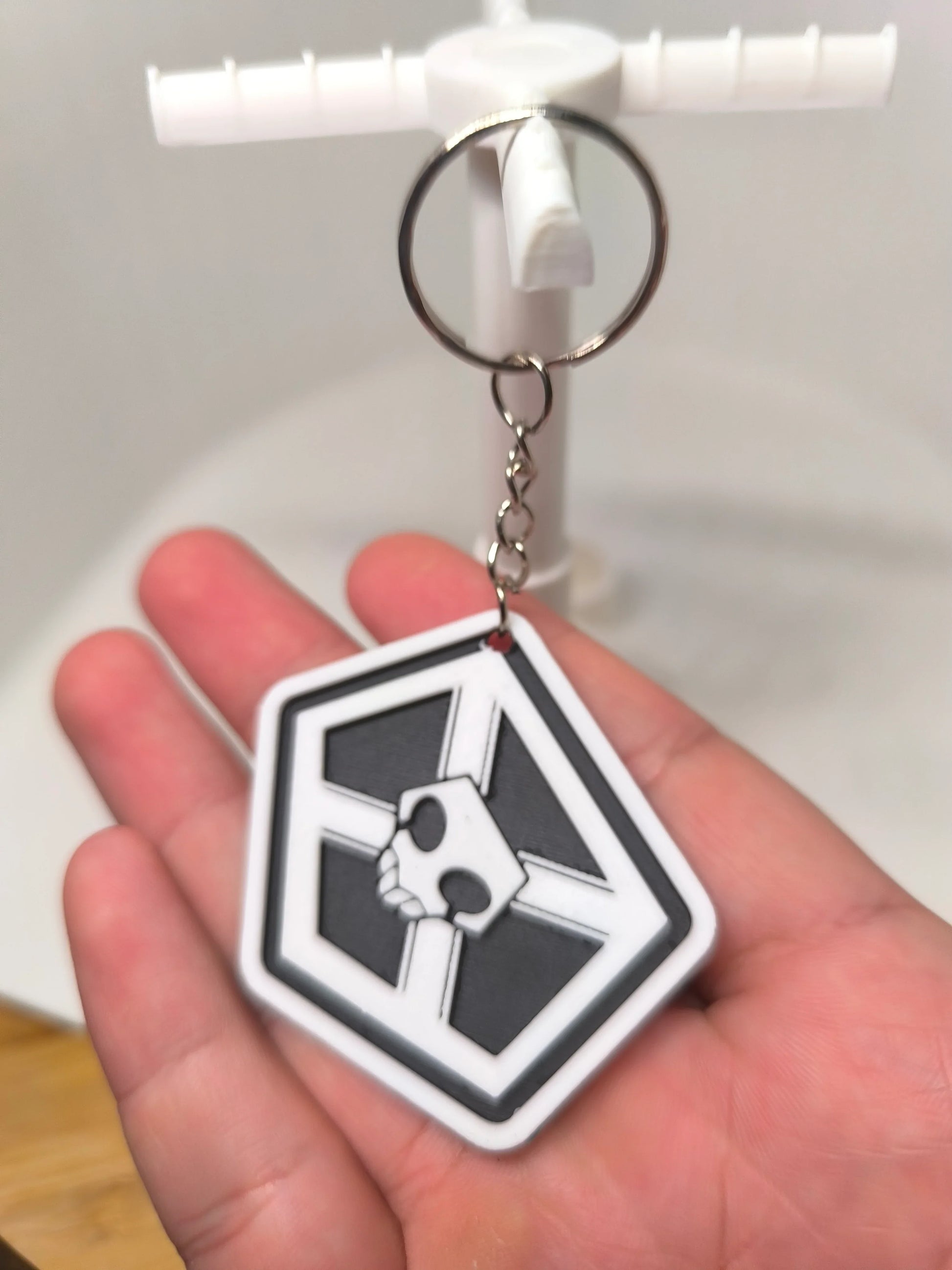 Porte-clés noir et blanc avec logo crâne géométrique tenu dans une main