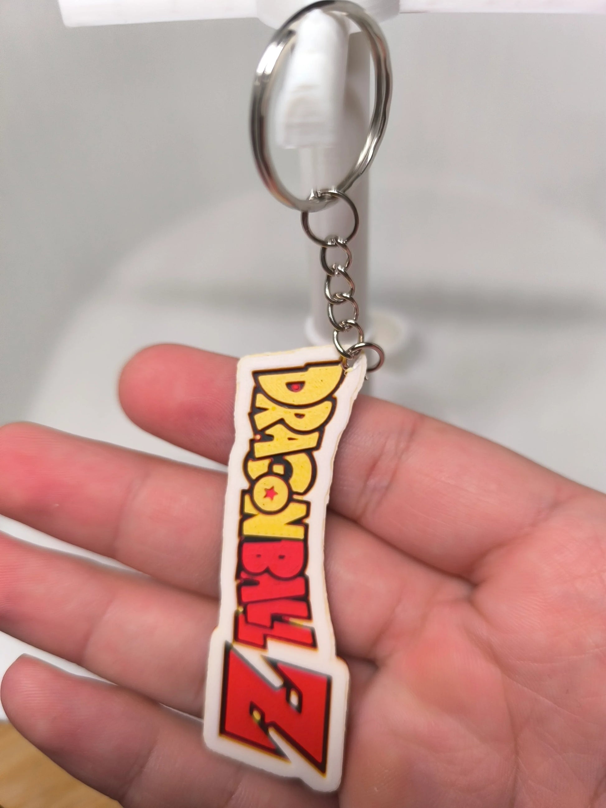 Porte-clés Dragon Ball Z avec logo coloré tenu dans une main, fond flou