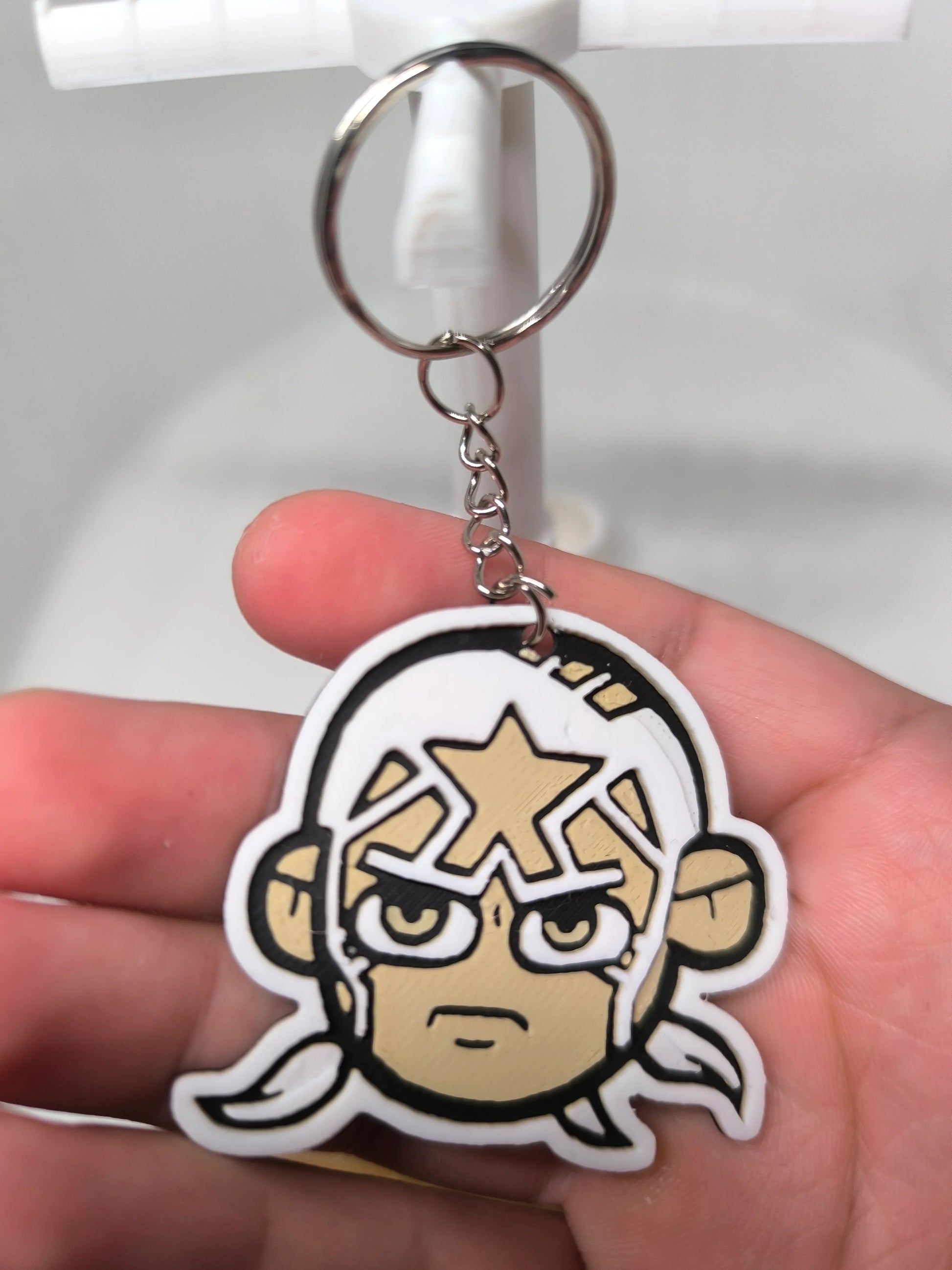 Porte-clés en caoutchouc avec visage stylisé et motif étoile, tenu dans une main humaine