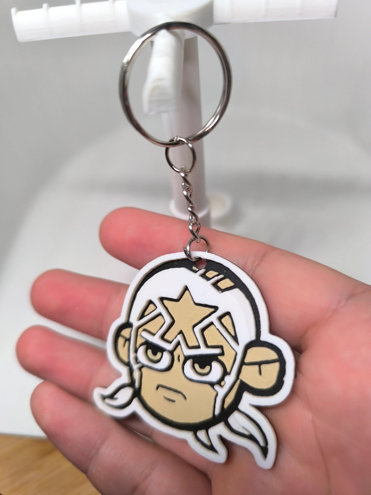 Porte-clés en PVC représentant un visage de personnage cartoon avec un masque blanc et une étoile dorée