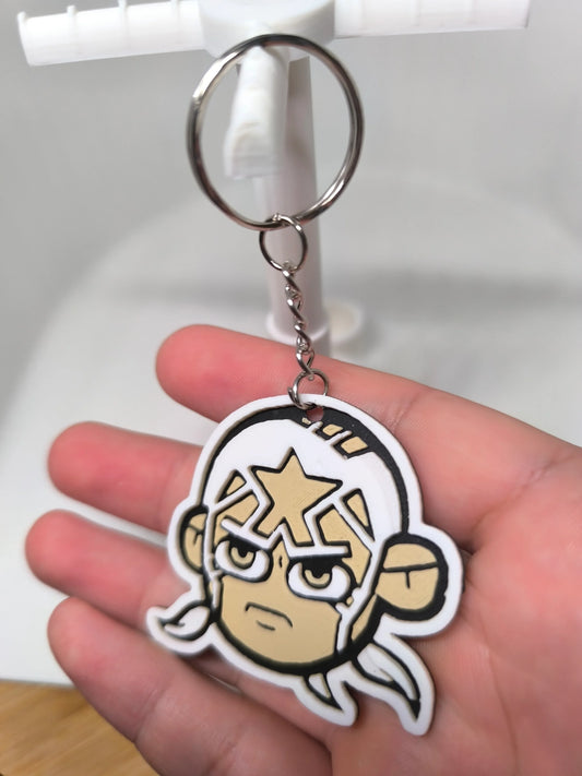 Porte-clés en PVC représentant un visage de personnage cartoon avec un masque blanc et une étoile dorée