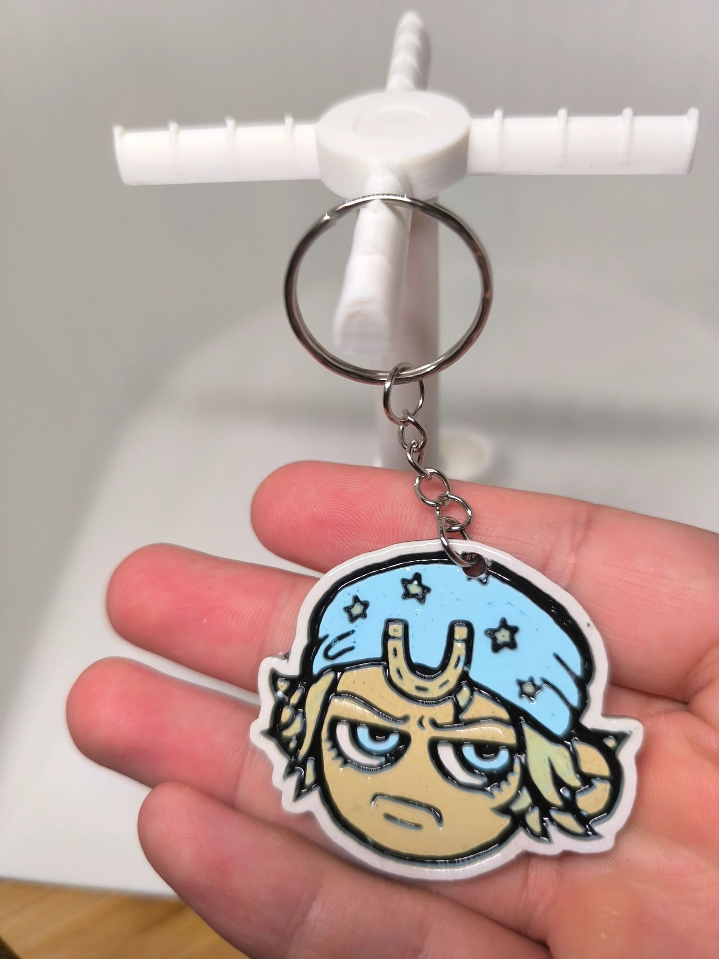 Porte-clés en plastique avec visage cartoon sérieux portant un bonnet bleu étoilé, tenu à la main