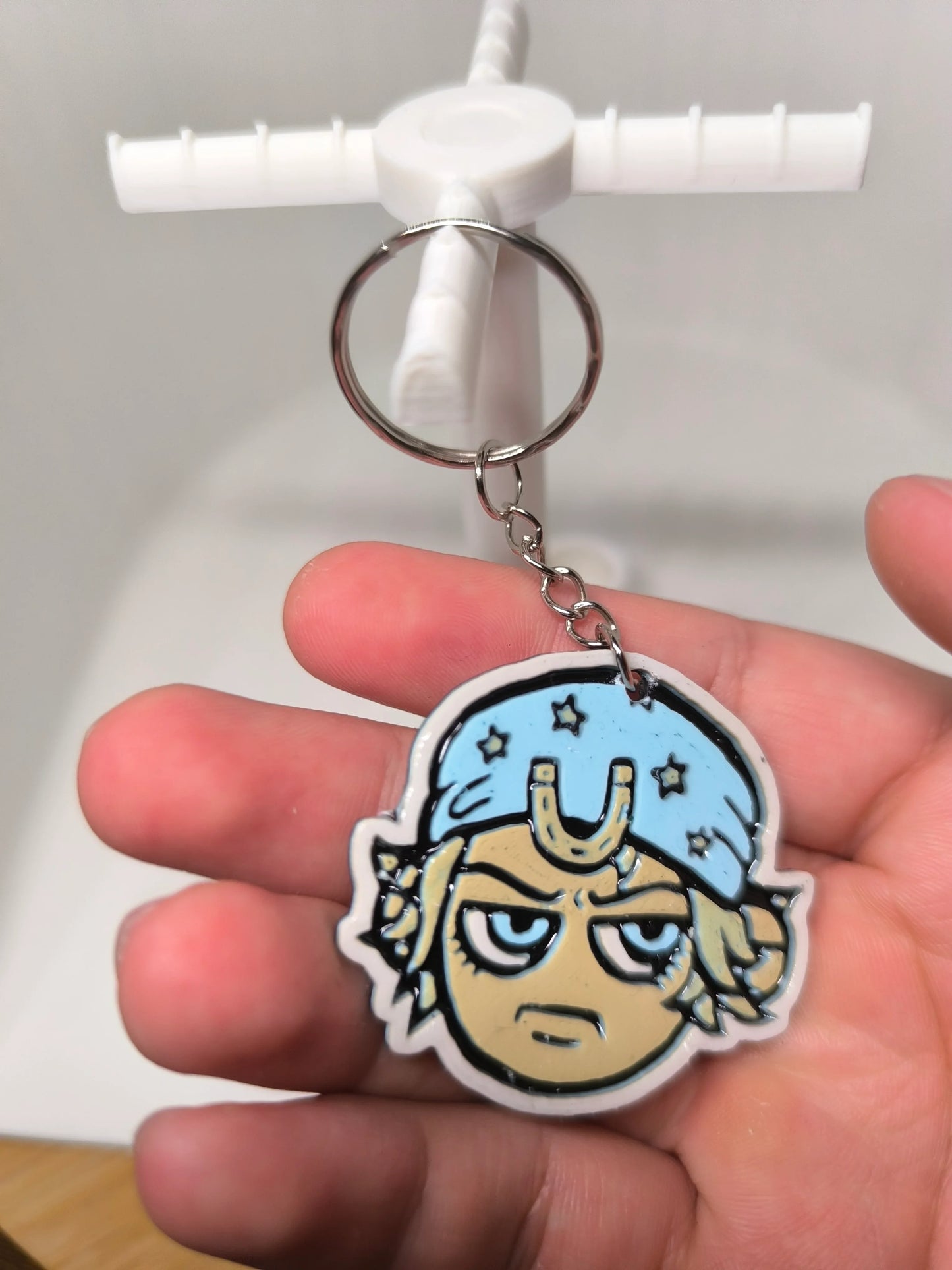 Porte-clés illustré d'un visage avec bonnet bleu étoilé et expression boudeuse tenu à la main