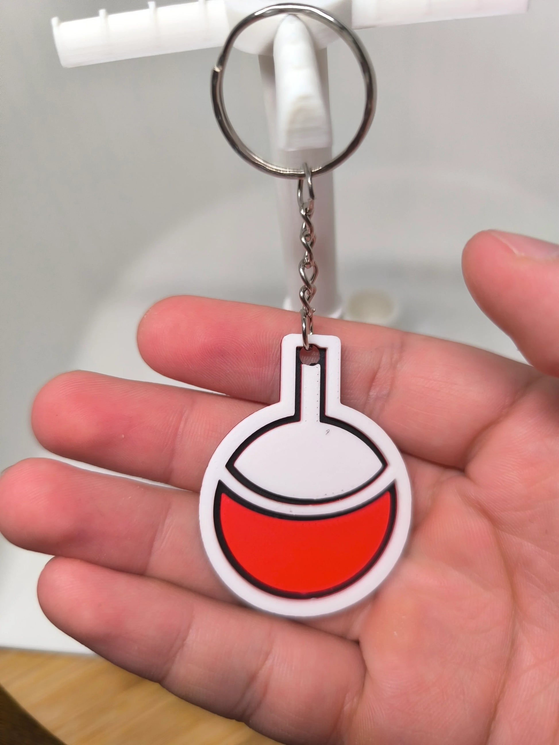 Porte-clés en silicone blanc et rouge en forme de fiole tenu dans une main