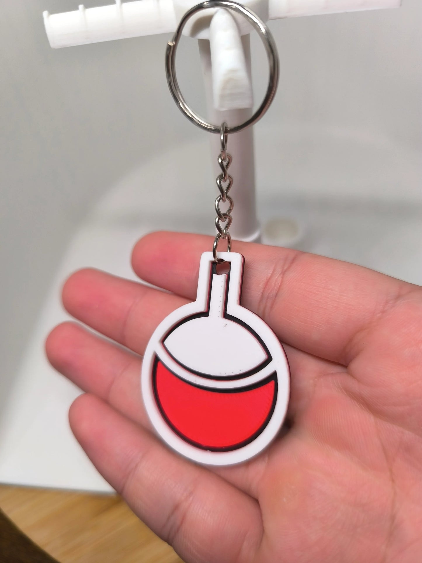 Porte-clés décoratif rond blanc et rouge tenu dans une main, fond bureau clair