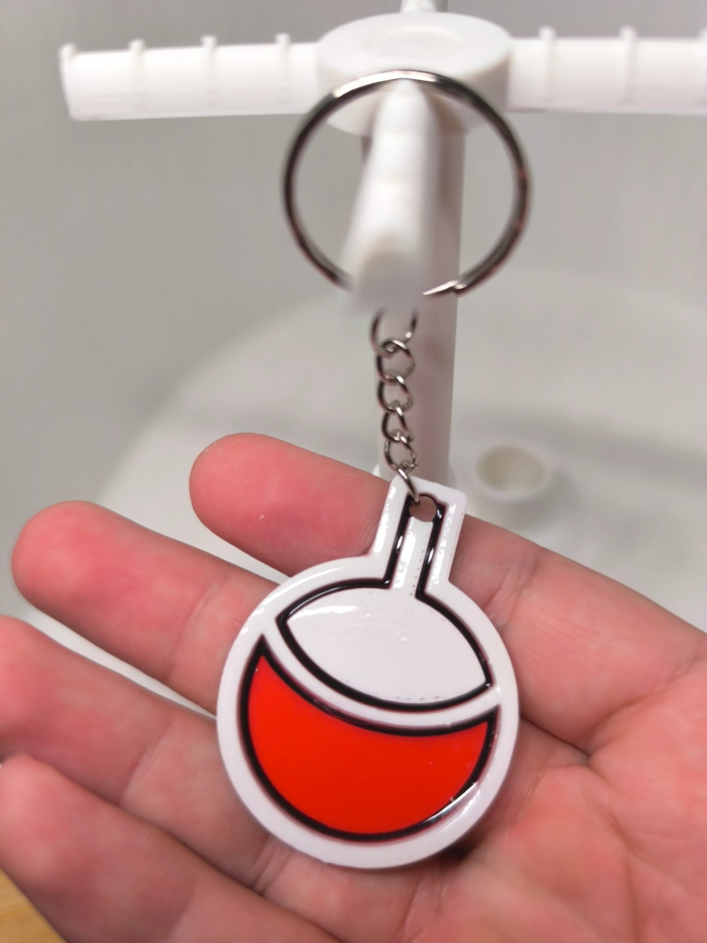 Porte-clés plastique blanc et rouge tenu à la main sur un support blanc flou