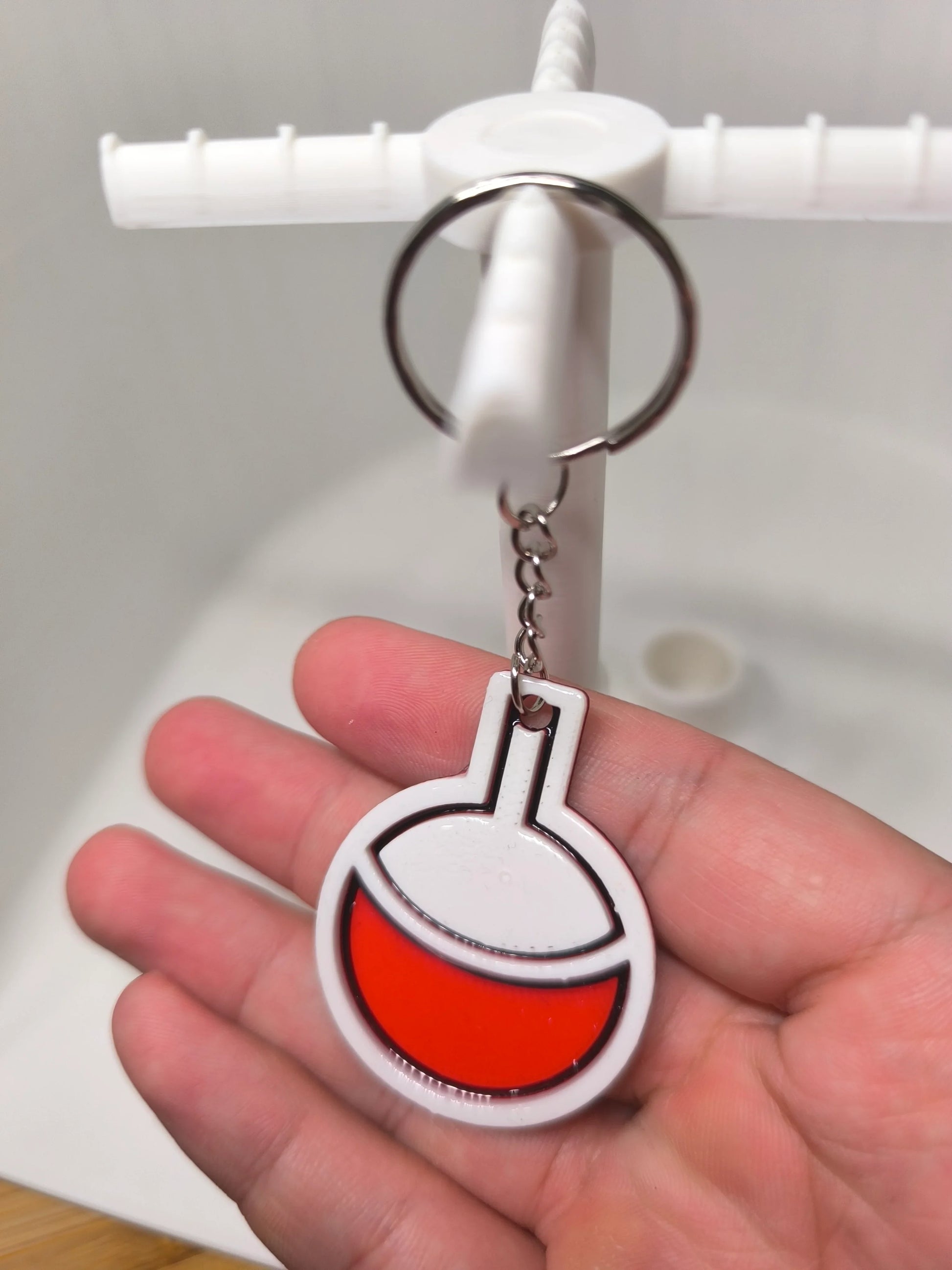 Porte-clés plastique blanc et rouge en forme de flotteur tenu dans une main devant un lavabo blanc