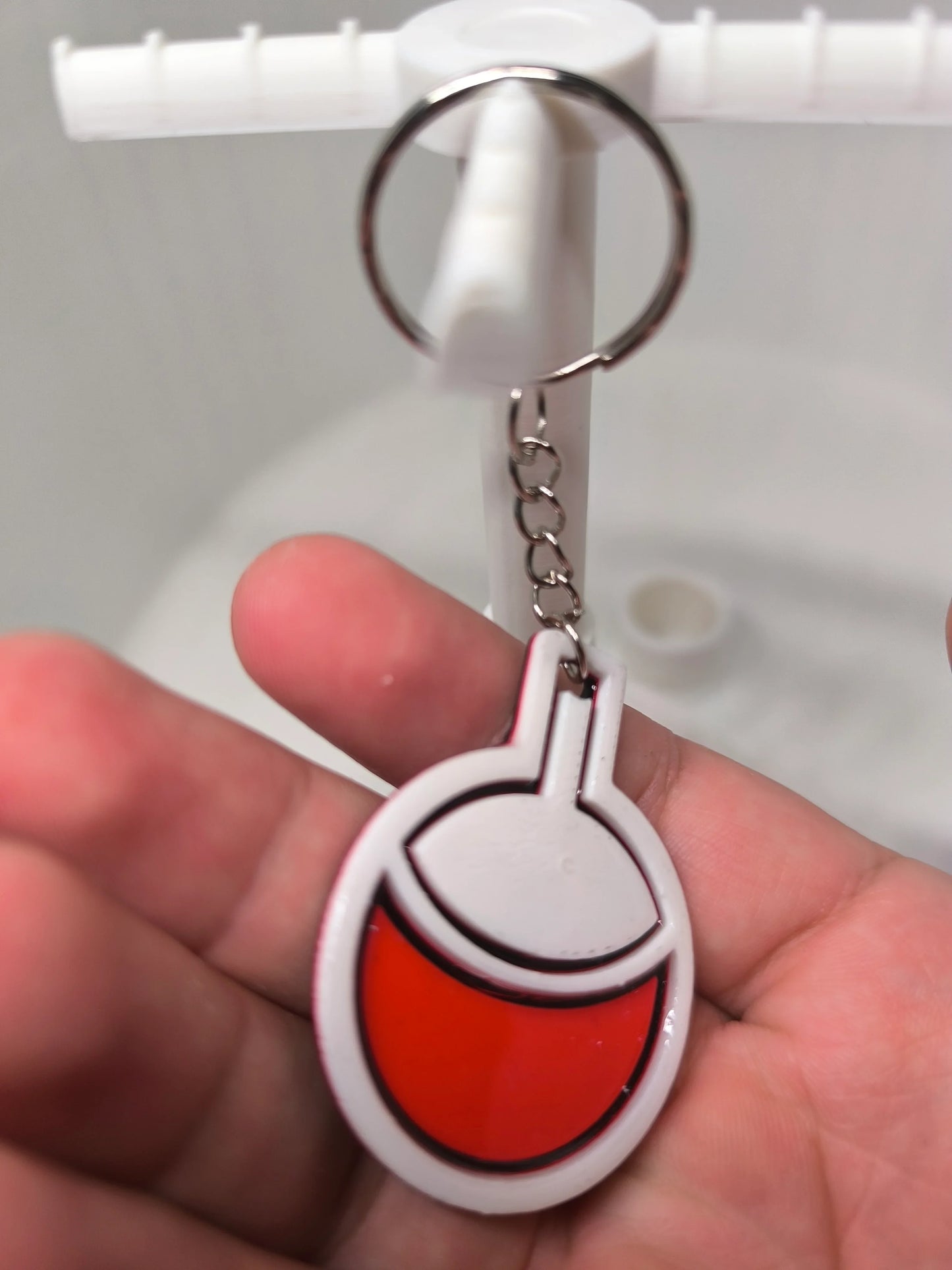 Porte-clés en forme de flotteur de pêche rouge et blanc tenu à la main sur fond flou