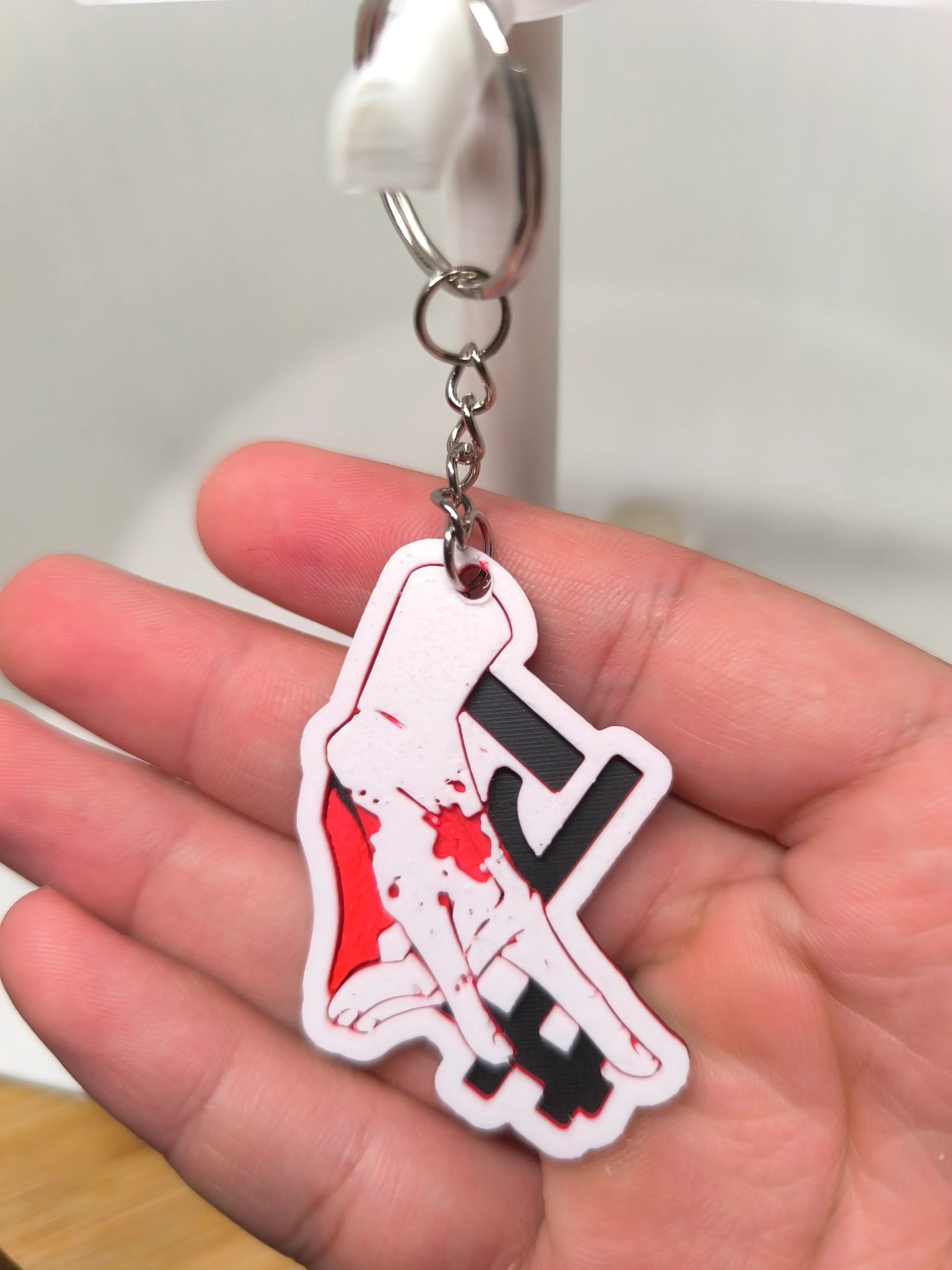 Porte-clés en plastique représentant une main blanche tenant un outil noir, tenu dans une paume