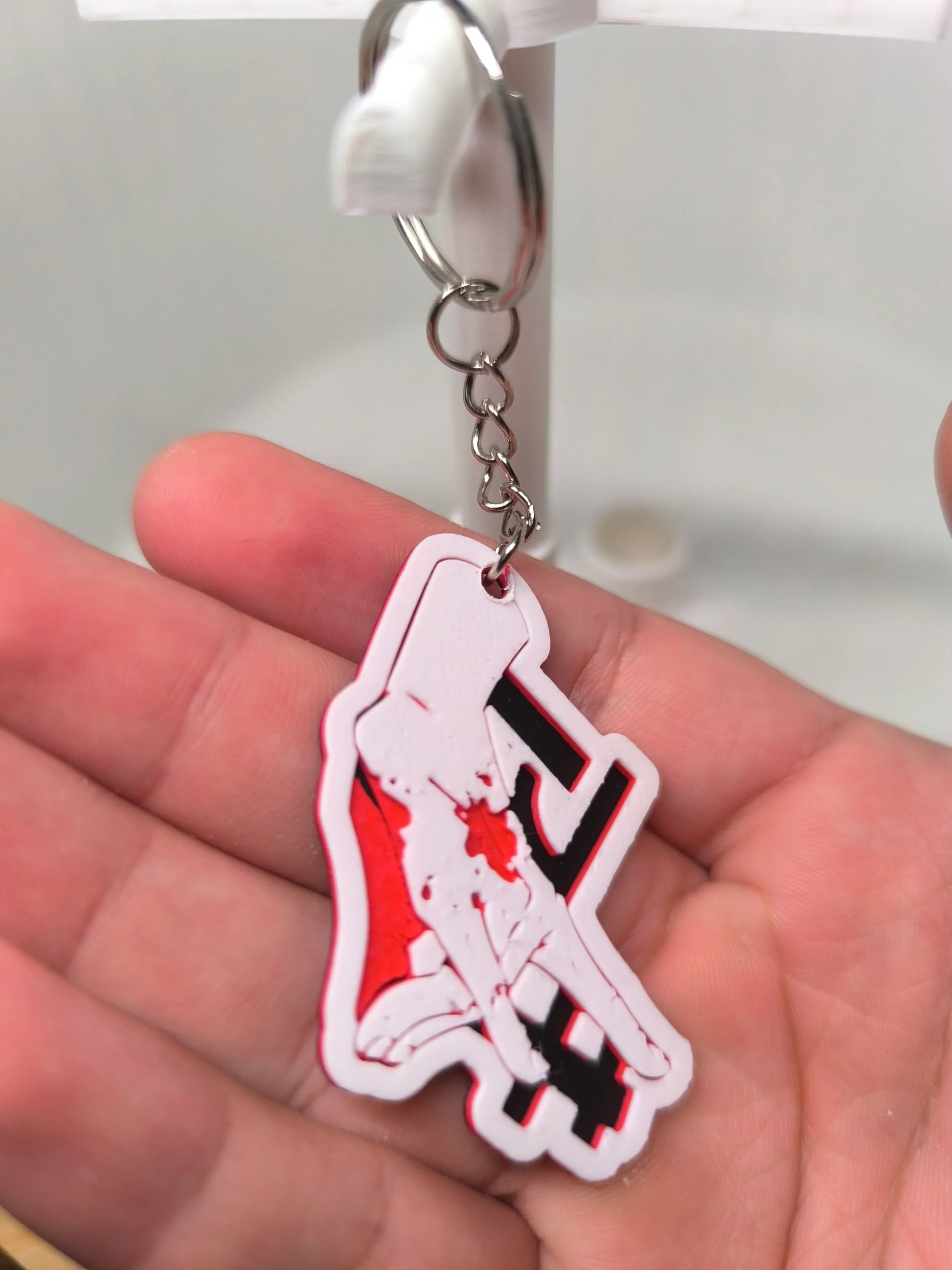 Porte-clés en PVC rouge et blanc avec design de mains tenant un symbole, tenu dans une main