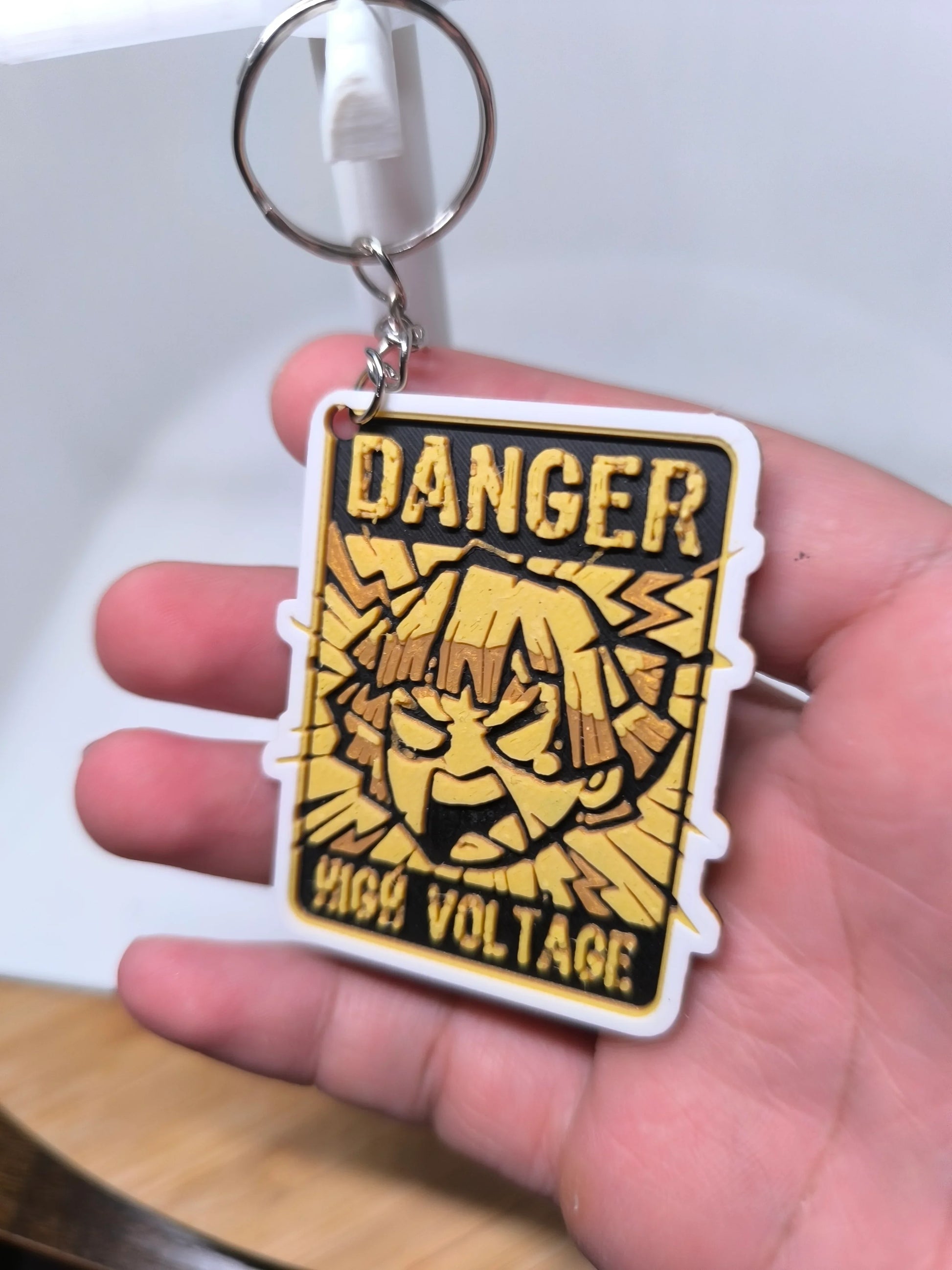 Porte-clés en plastique jaune et noir avec texte Danger High Voltage et visage stylisé en colère