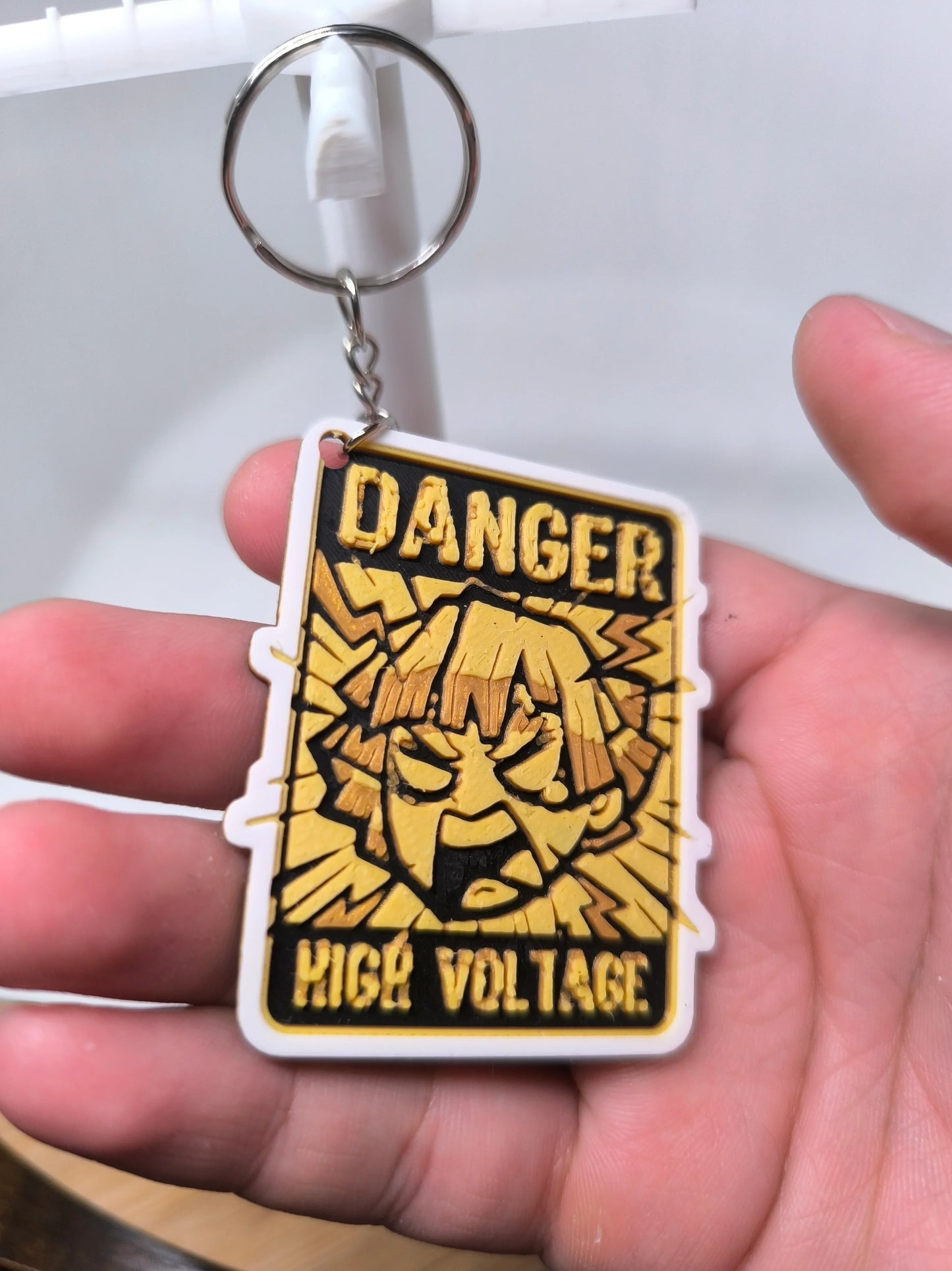 Porte-clés avec symbole danger haute tension jaune et noir tenu dans une main