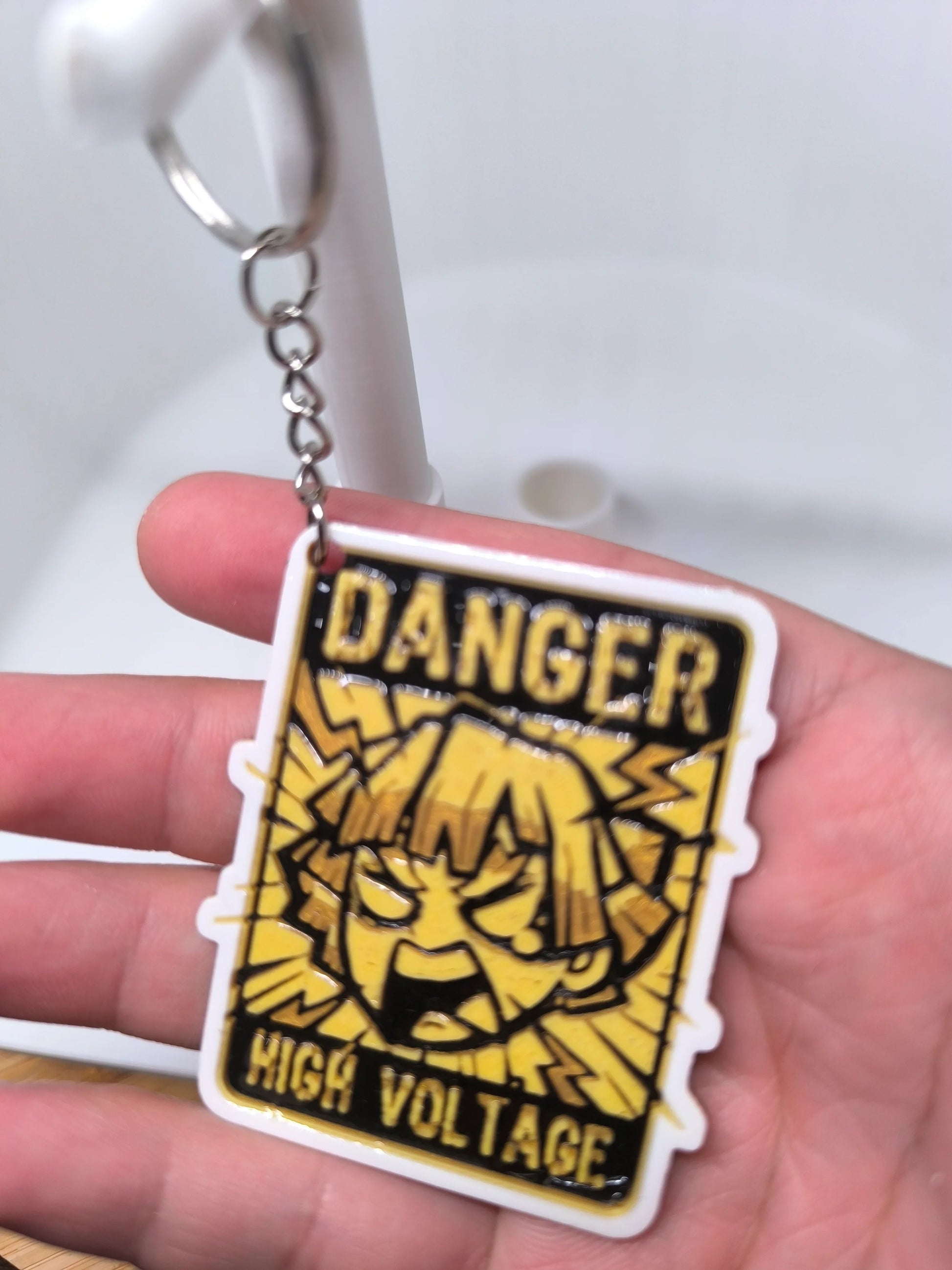 Porte-clés jaune et noir avec texte "Danger High Voltage" et illustration style manga 