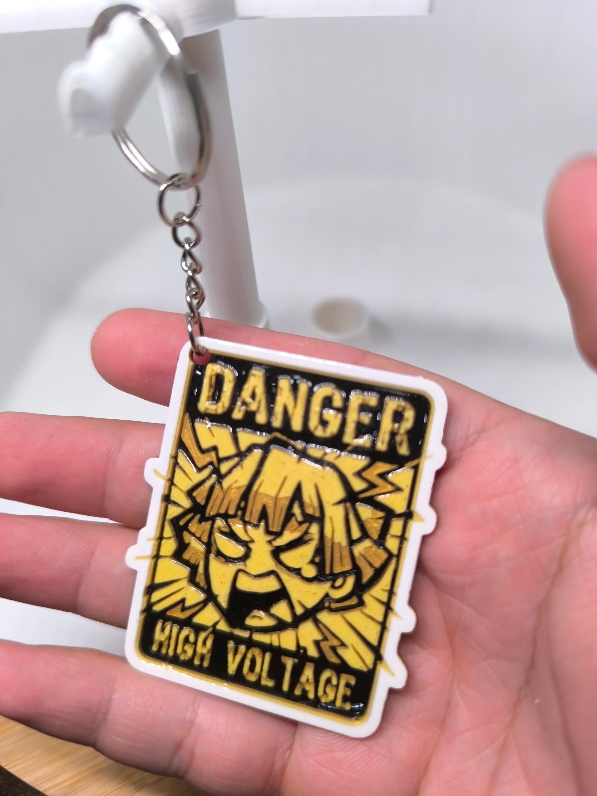 Porte-clés jaune avec dessin animé et texte Danger High Voltage tenu dans une main