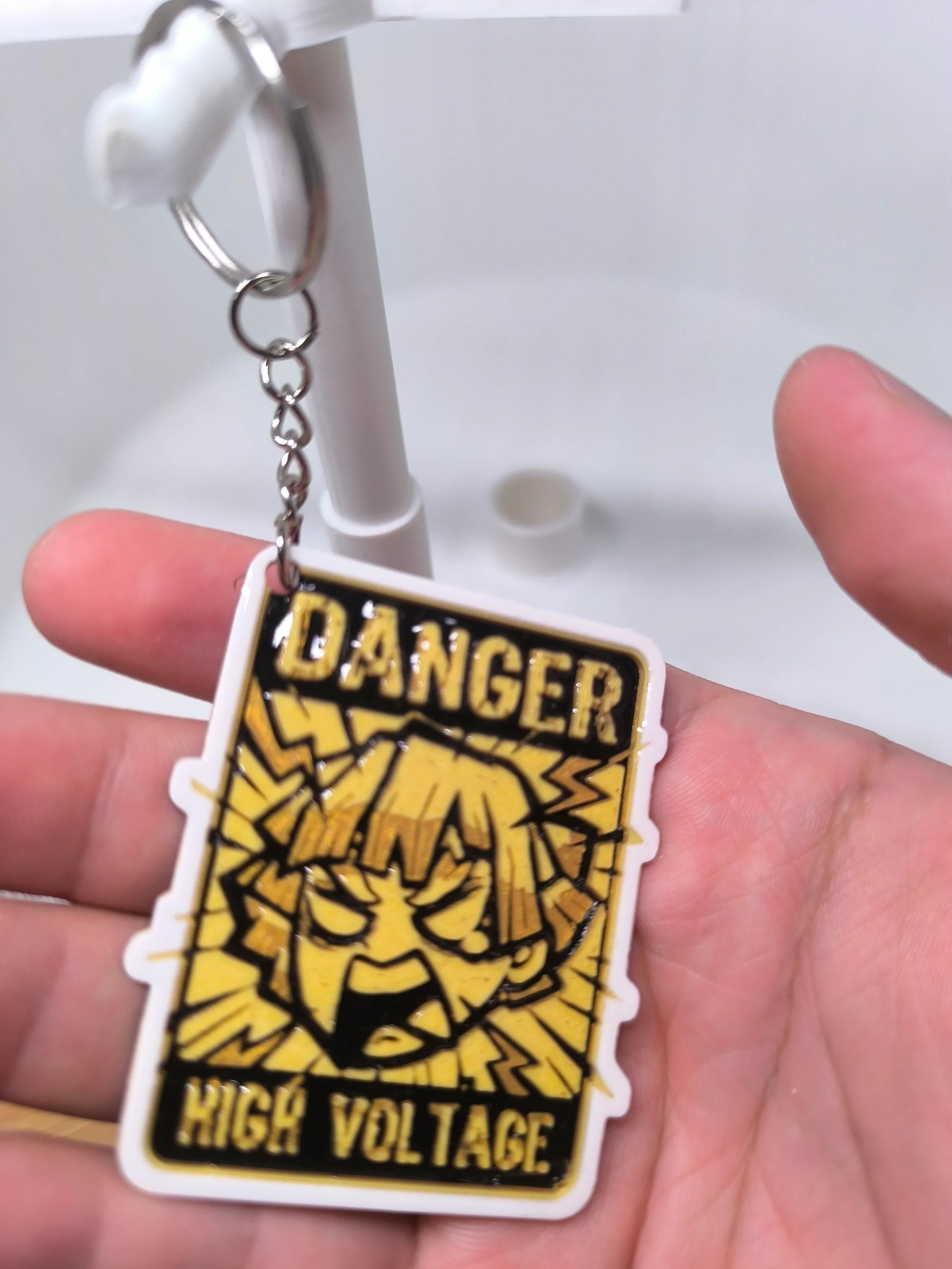 Porte-clés carré avec illustration jaune et noire style manga, texte Danger High Voltage