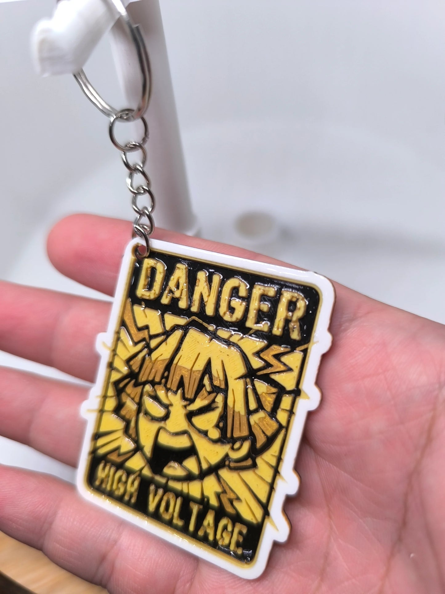 Porte-clés jaune et noir avec inscrit Danger High Voltage et visage dessiné en colère
