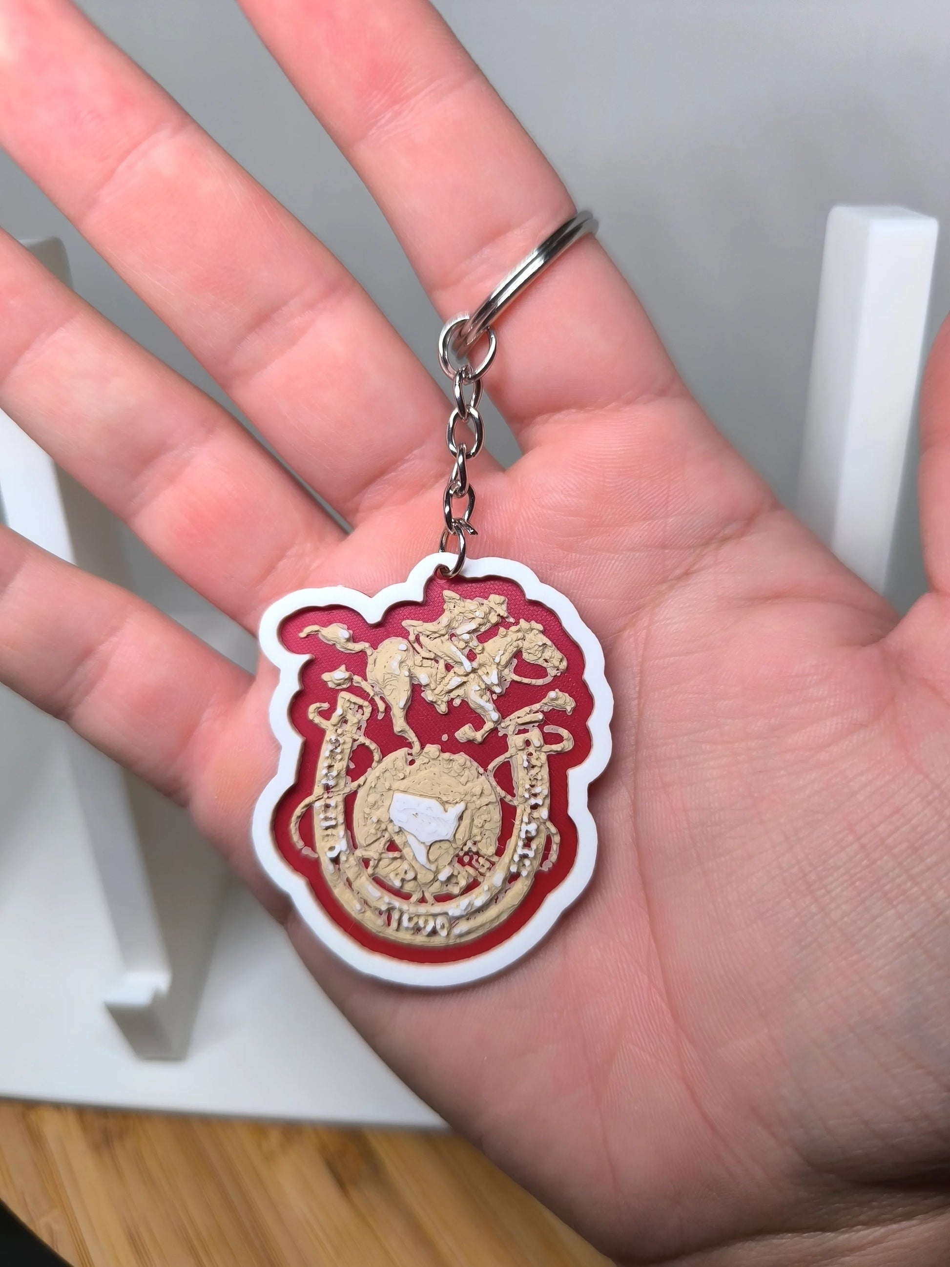Porte-clés rouge et doré avec motif de cavalier à cheval tenu dans une main