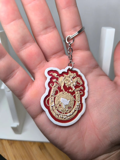 Porte-clés rouge et blanc avec blason doré tenu dans une main, fond flou bois et blanc