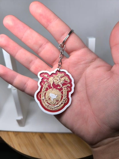 Porte-clés en relief doré sur fond rouge tenu dans une main, décor cheval et fer à cheval