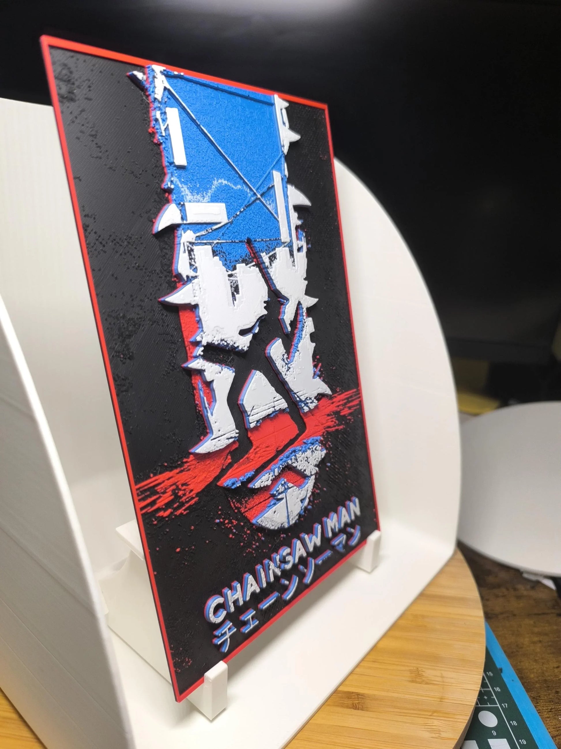 Plaque décorative Chainsaw Man avec illustration stylisée et texte en anglais et japonais, fond noir et accents rouges et bleus